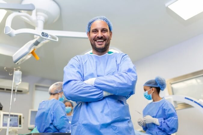 Portrait of male surgeon in operation theater looking at camera. Doctor in scrubs and medical mask in modern hospital operating room.